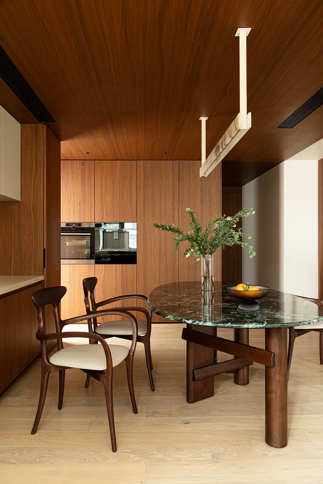 A minimalist kitchen with wood cabinets, marble countertops, and a round dining table with white chairs.
