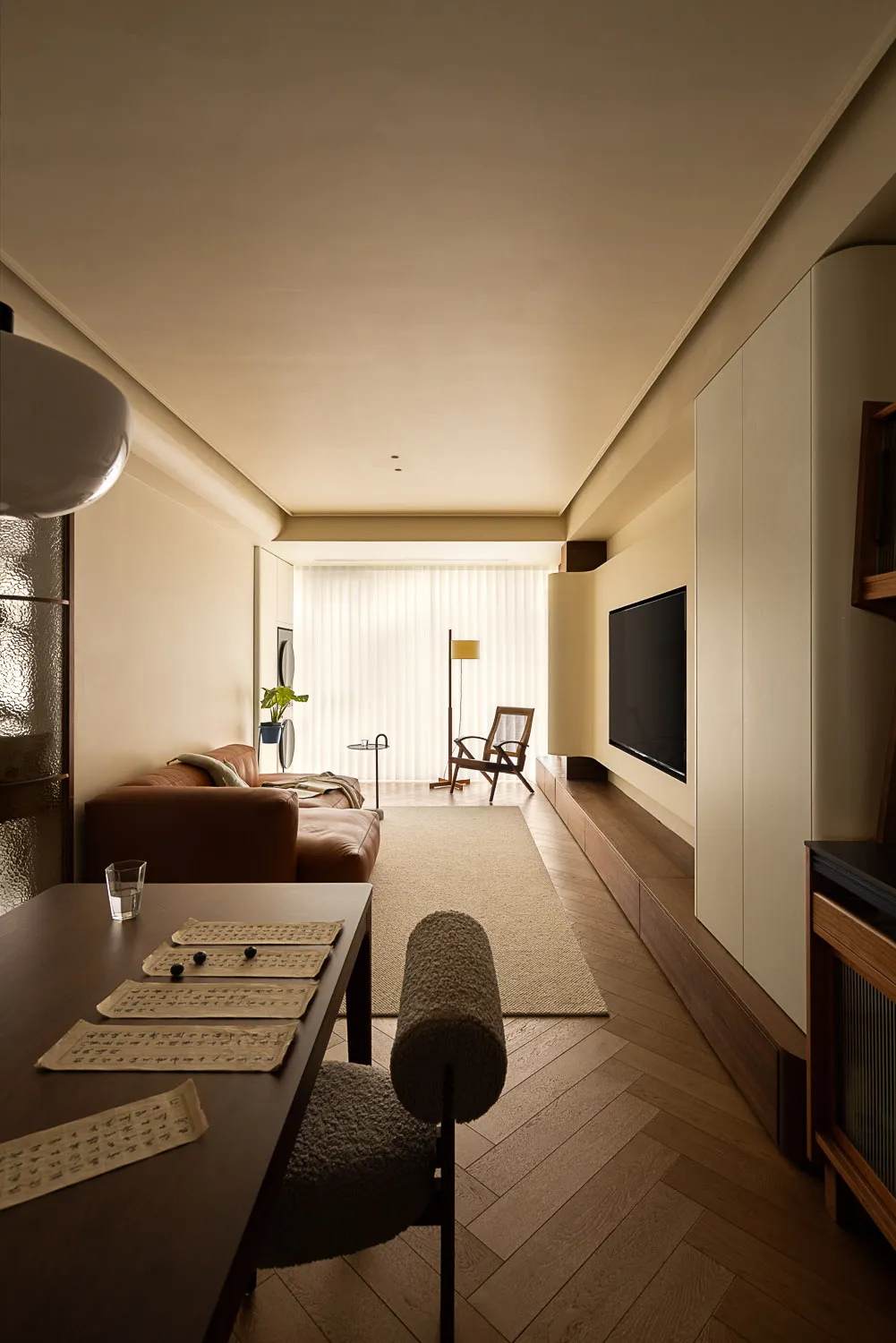 A minimalist living room featuring wooden furniture, a leather sofa, and a flat-screen TV mounted on a wall with built-in sto