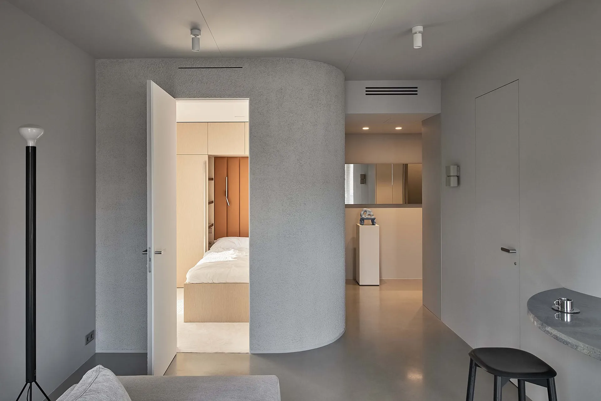 A modern bedroom with a concrete wall, minimalist design, and a bed with white bedding.