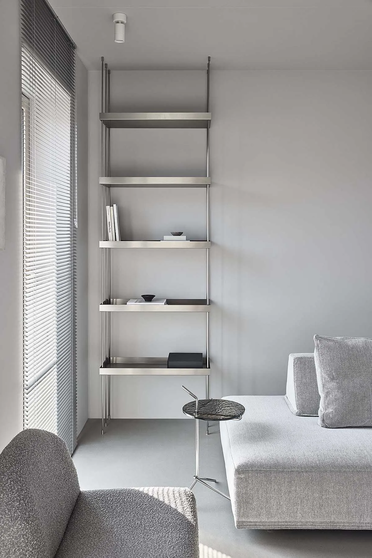 A modern interior design featuring minimalist metal shelving unit against a gray wall and a gray sofa with a side table.
