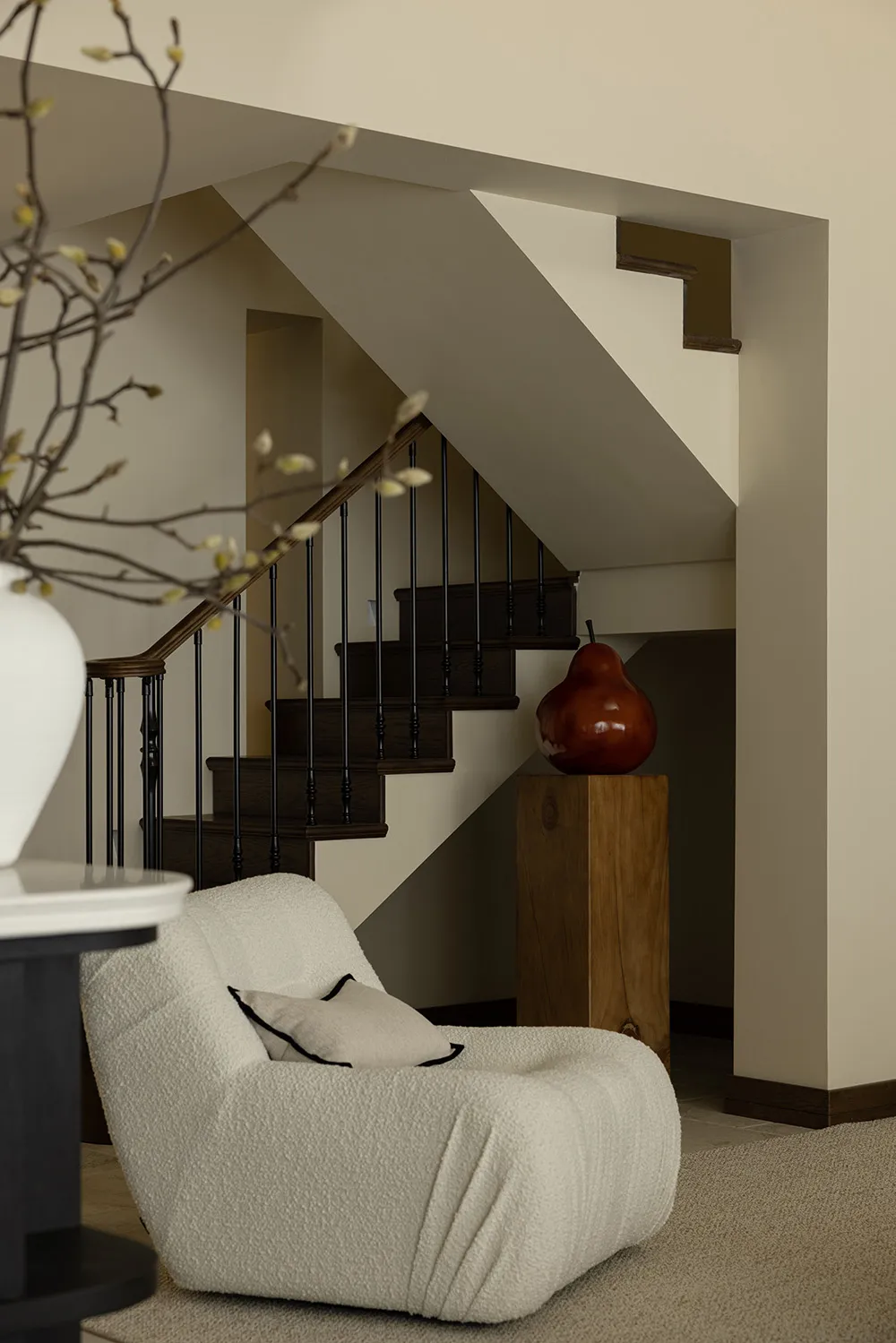 A cozy residential staircase with wooden steps and black railings, featuring a modern, plush armchair and a red pear sculptur