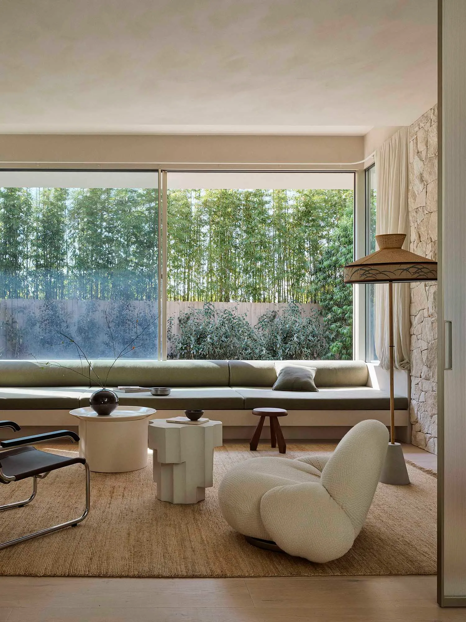 A cozy minimalist living room with a built-in sofa, fabric cushions, and stone accents, featuring floor-to-ceiling windows wi