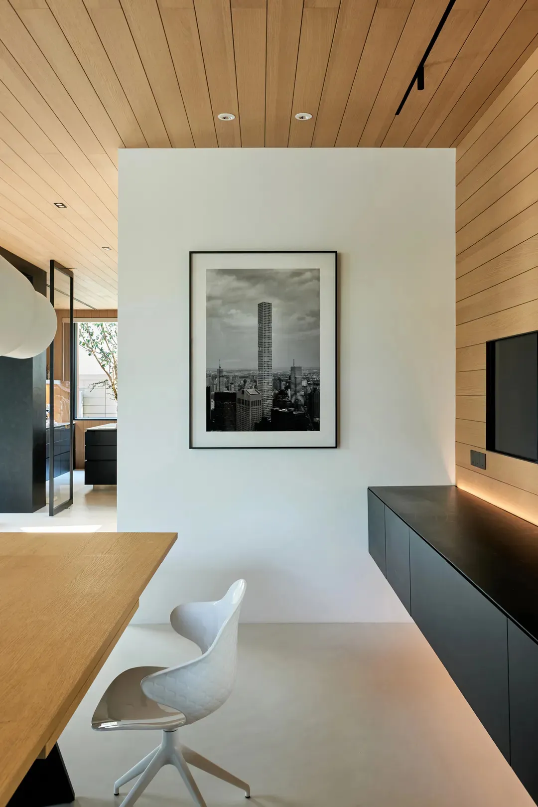 A home office with a modern design featuring a white chair and a wooden desk, with a black and white photograph of a cityscap