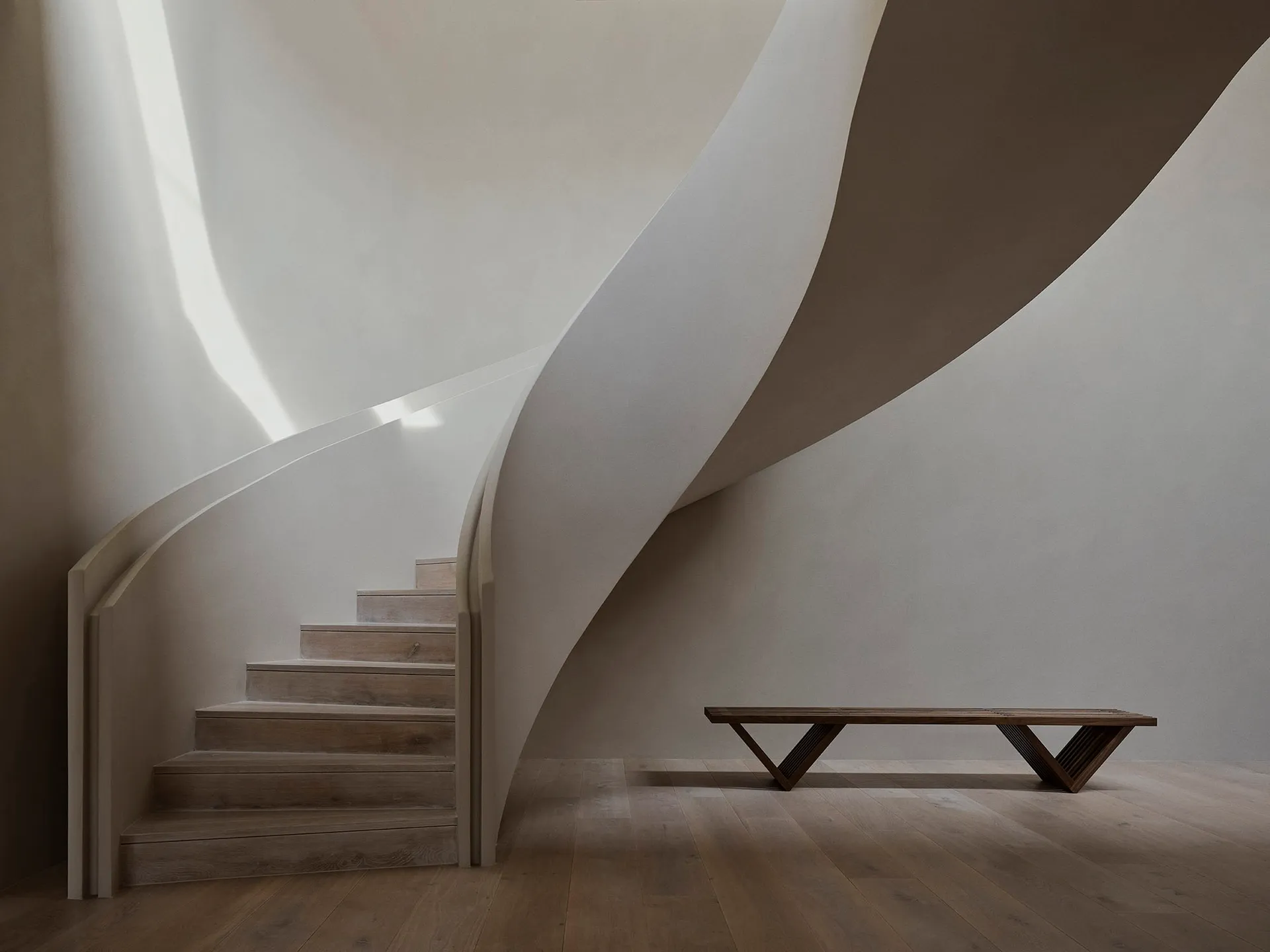 A modern interior with a sleek, curving staircase made of tukey wood. The space features minimalist design and light-colored