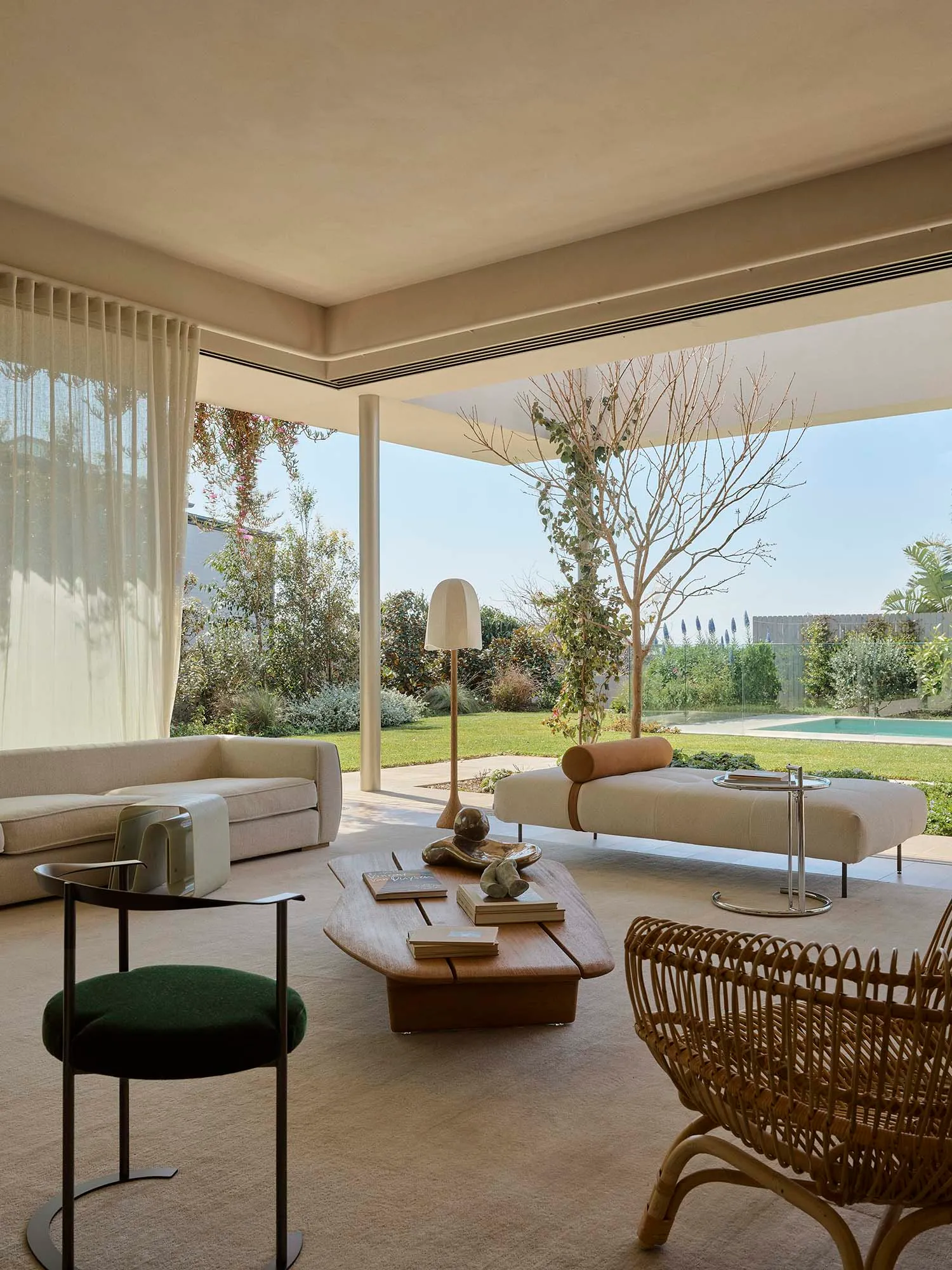 Modern living room featuring a woven armchair, fabric sofa, wooden table, and glass lamp. Bright, spacious, and contemporary.