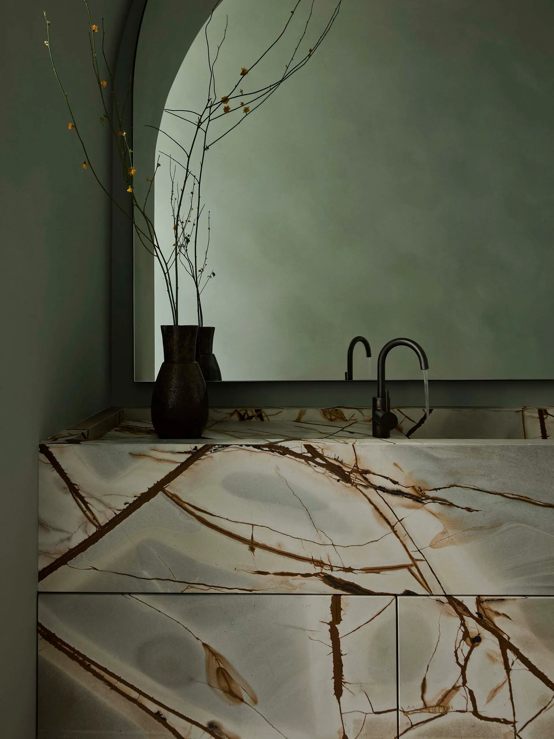 Modern bathroom with a marble countertop featuring dark veins, a black faucet, and a vase with dried branches on a circular w