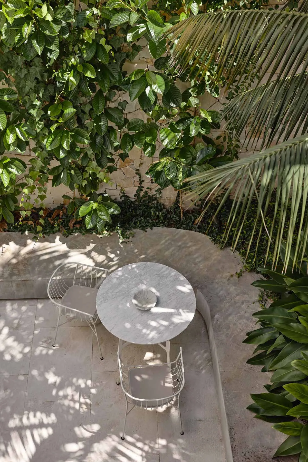 A minimalist outdoor seating area featuring a round concrete table and two matching chairs.