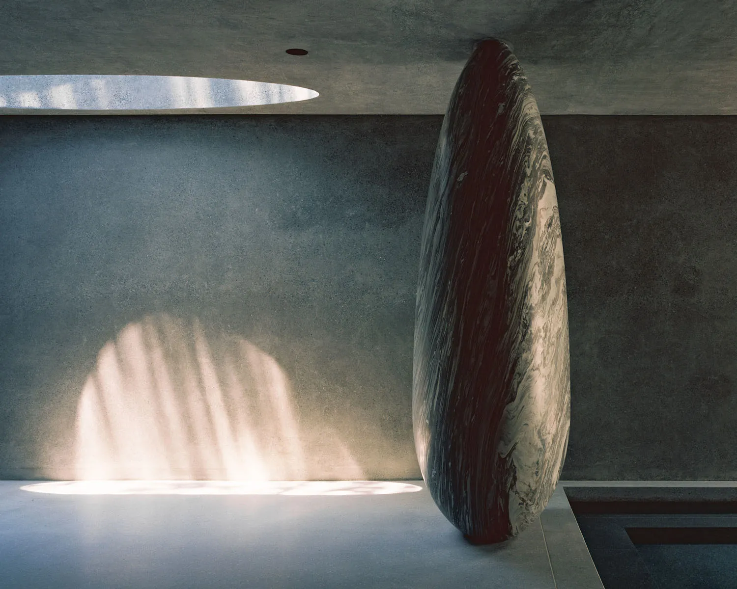 A tall, black and white marble vase situated in a modern interior space, casting a shadow on the wall.
