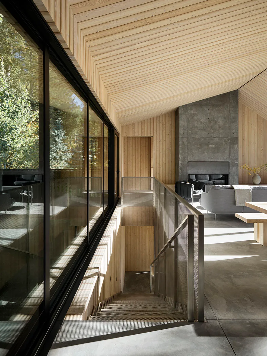 Modern minimalist interior design with wood, concrete, and glass materials in a cabin setting.
