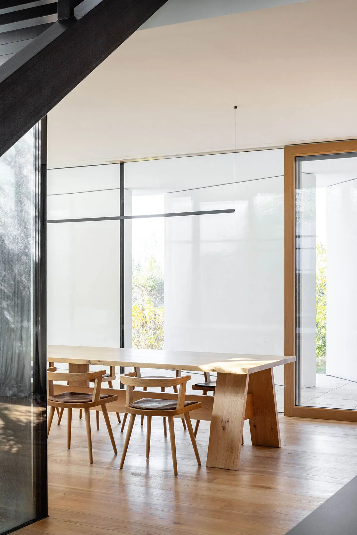 Modern minimalist living and dining area with wooden furniture and large glass windows.