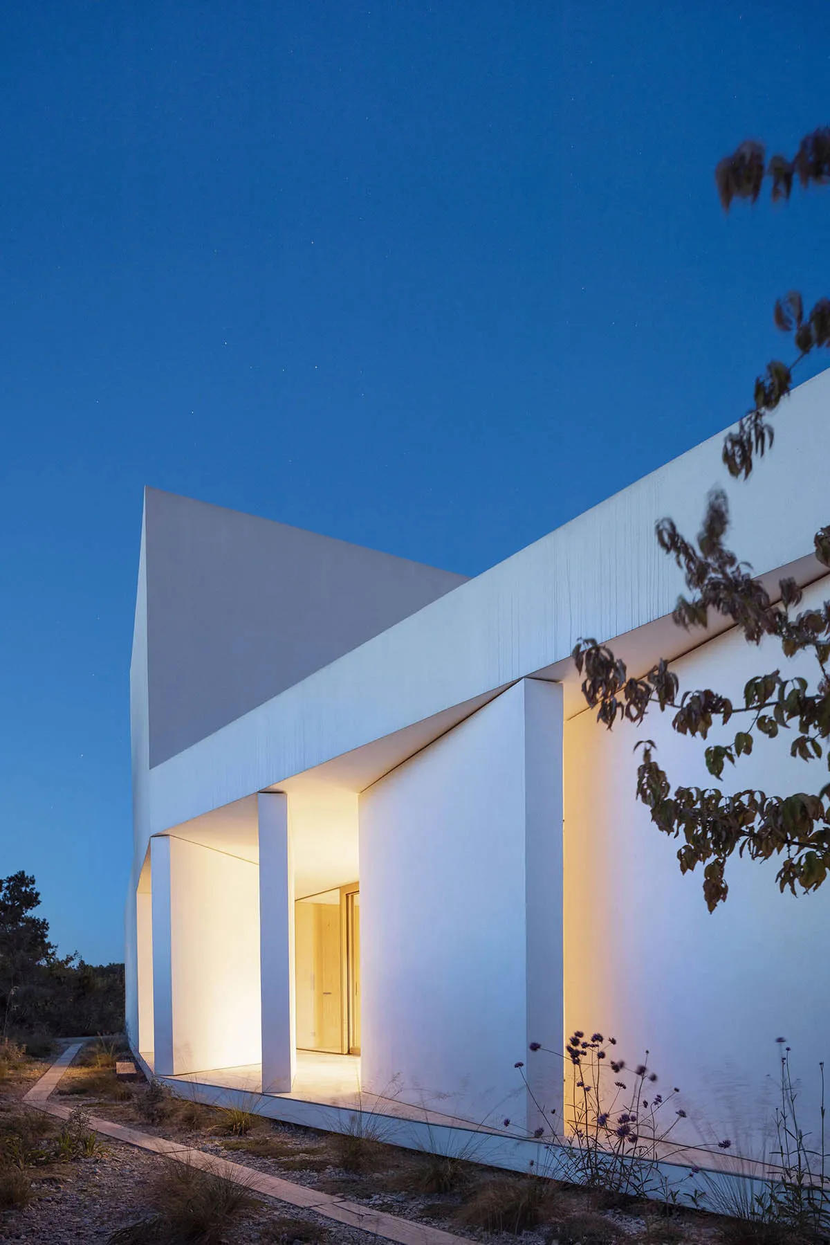 A minimalist white house with prominent white walls and a clear blue sky in the background.