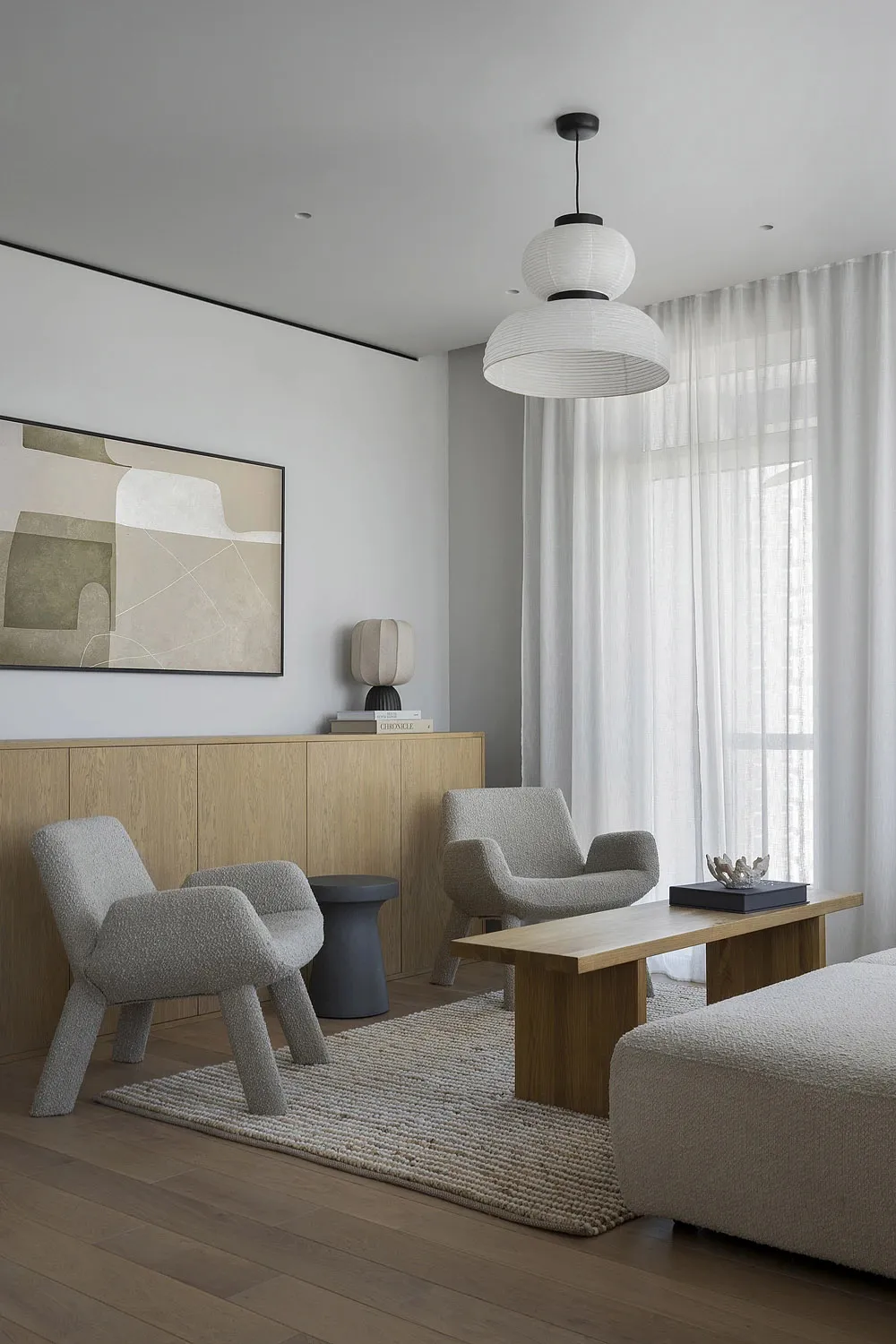 A modern minimalist living room with two gray armchairs, a wooden coffee table, and a wooden cabinet.