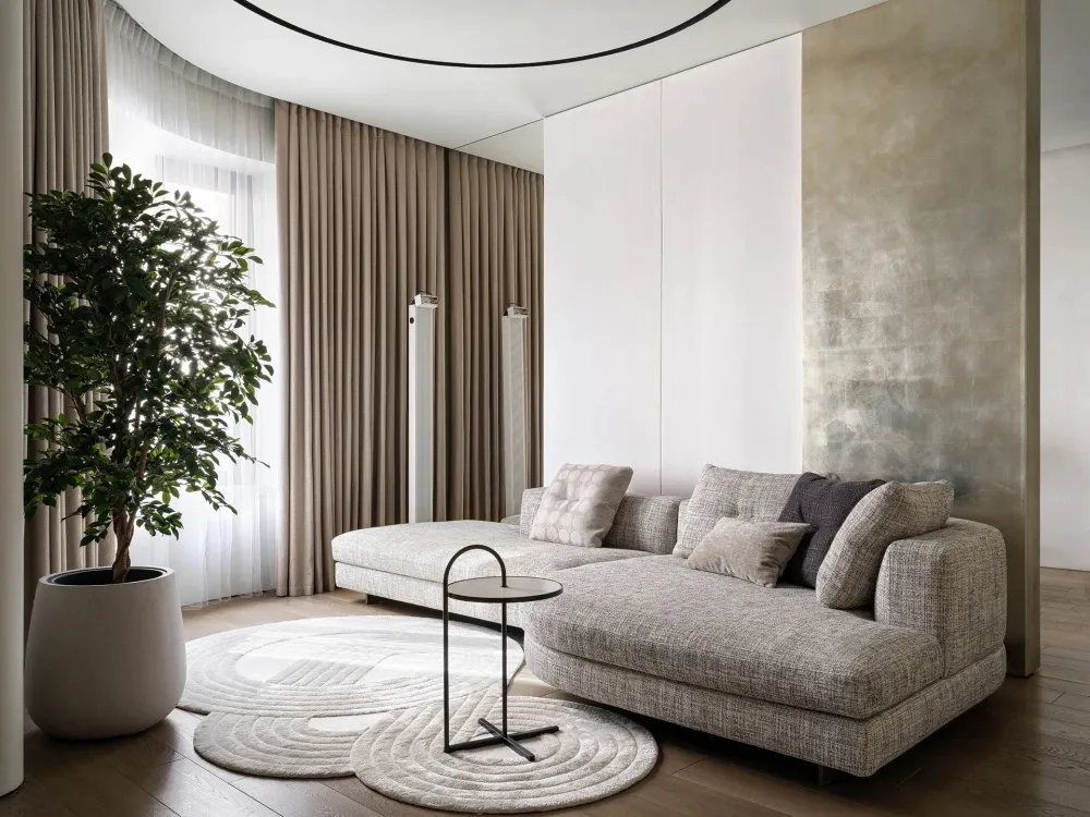 A modern, minimalist living room with a grey sofa, white curtains, and a concrete wall.