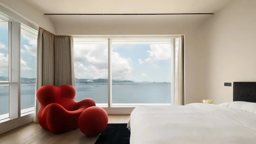 A minimalist bedroom with a glass window overlooking the ocean.