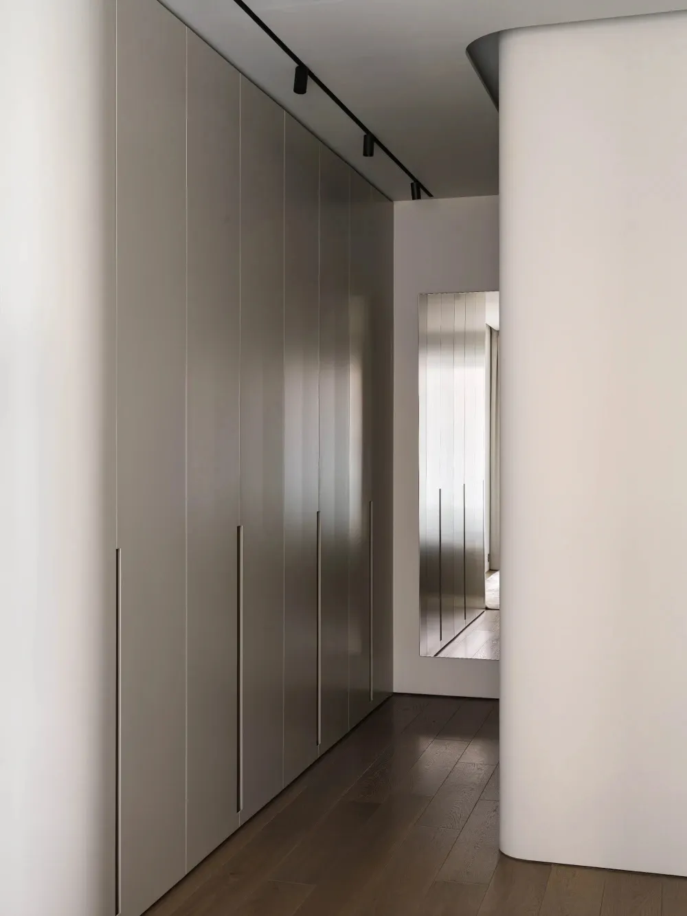 Modern minimalist bedroom with white cabinets and wooden flooring.