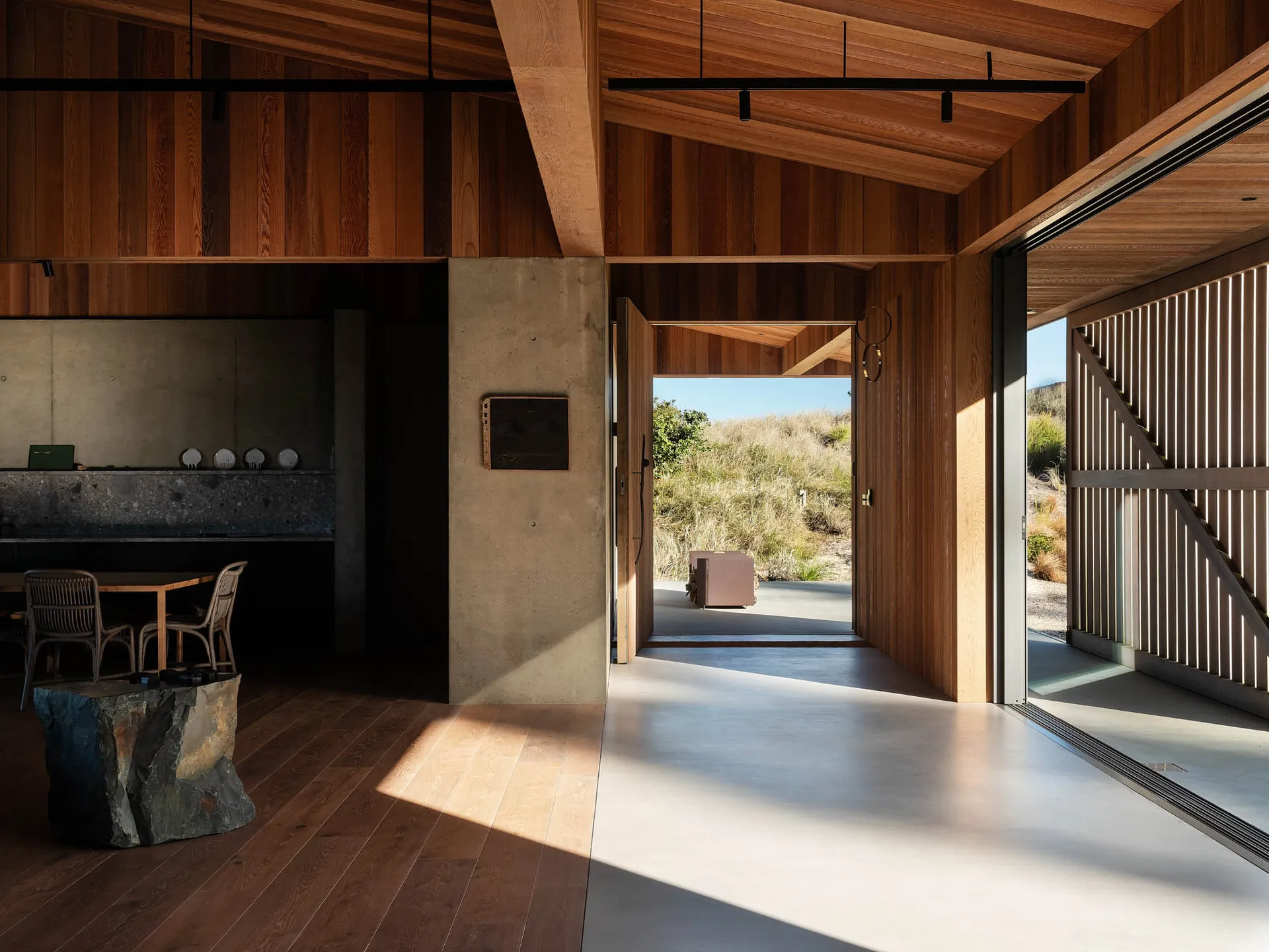 Modern residential interior featuring exposed wood beams, concrete flooring, and a natural outdoor view through large windows