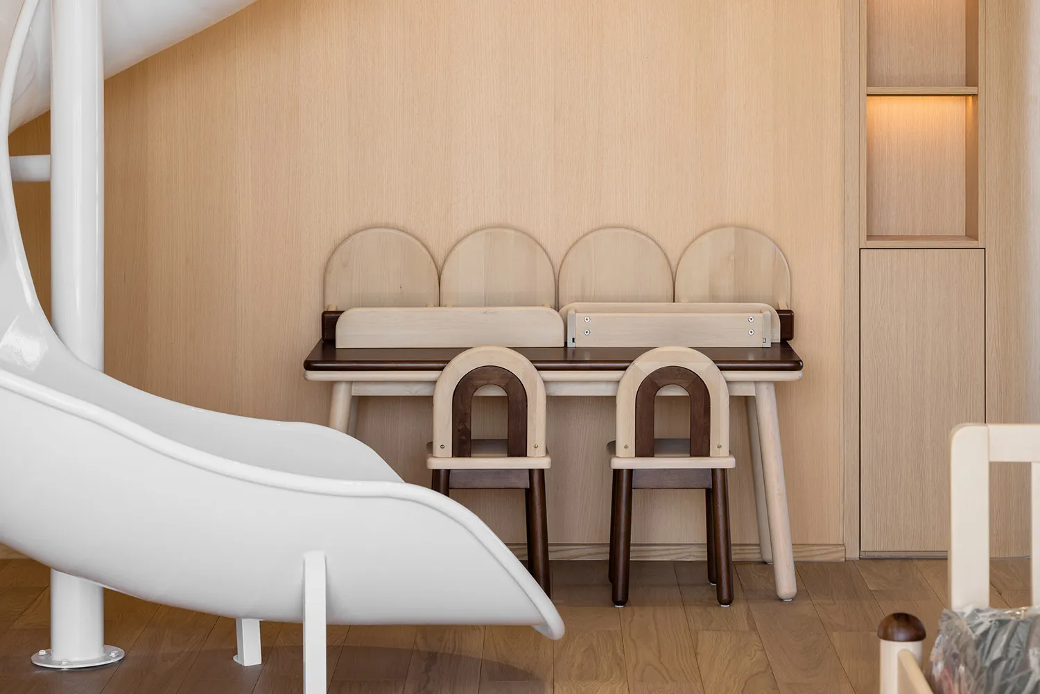 A minimalist children's playroom featuring wooden furniture and a white slide.