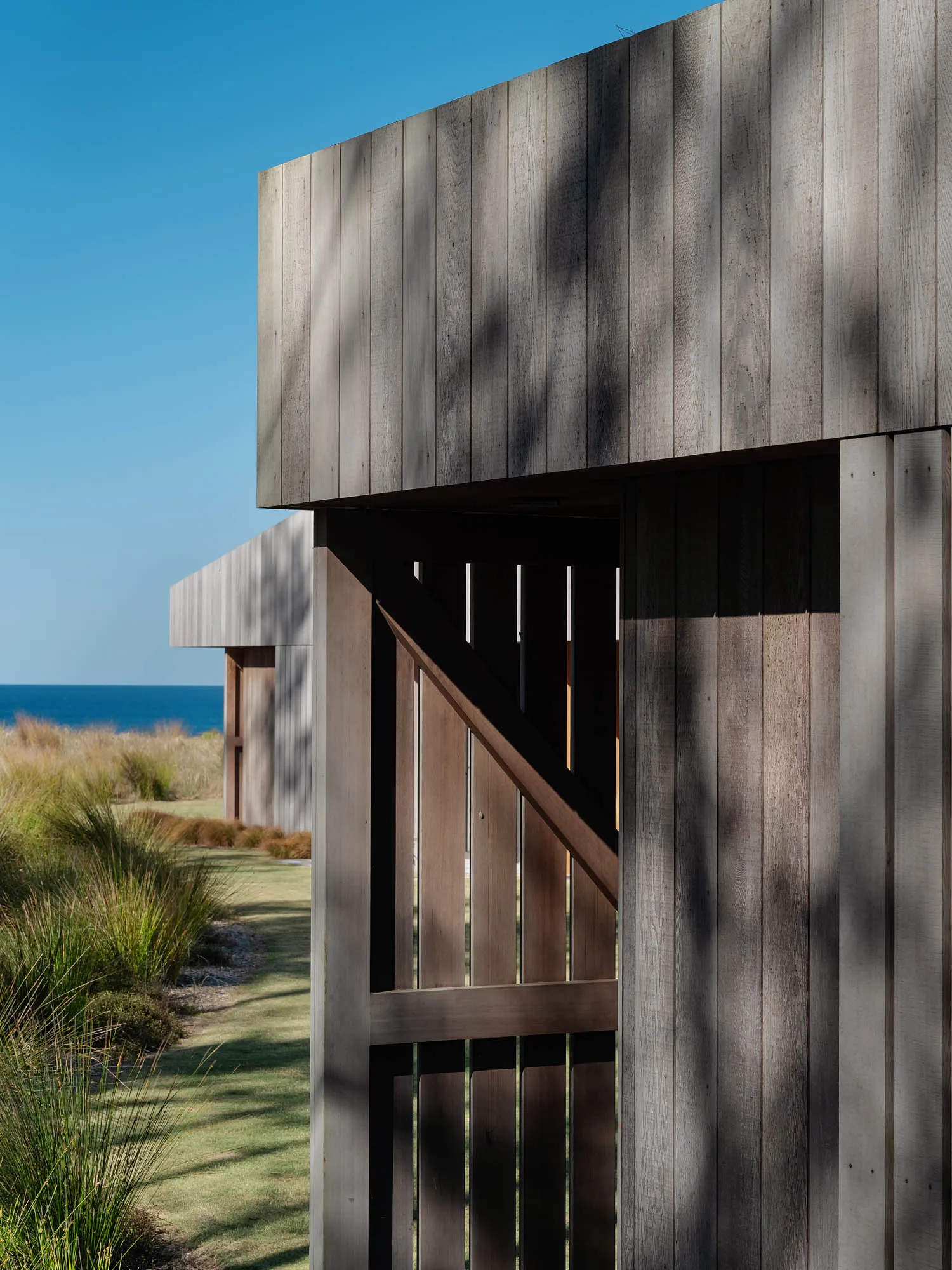A modern entryway with a wooden facade and gate, featuring natural light and a clear sky in the background.