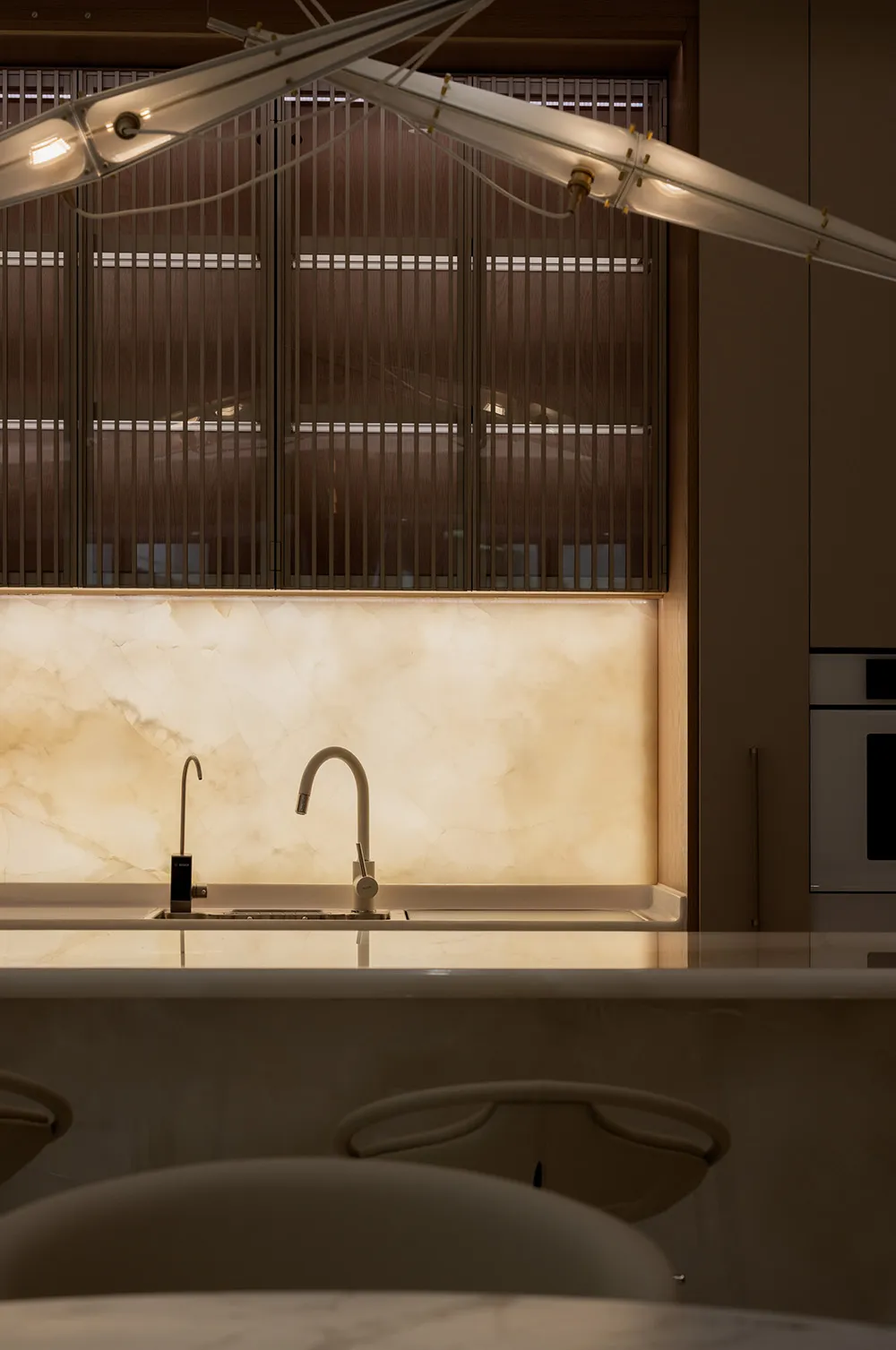 A minimalist modern kitchen featuring marble countertops and backsplash with a sleek, white faucet and lighting design above.