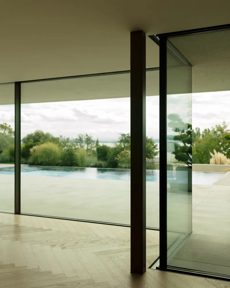 A modern glass window overlooking a serene outdoor space and pool, framed by minimal interior design.