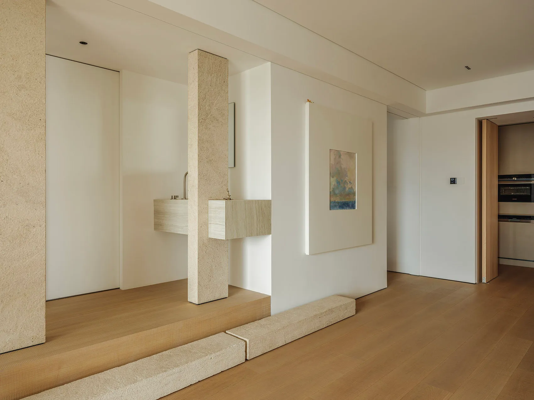 Modern residential entryway with minimalist design, featuring a concrete pillar and wood floor.