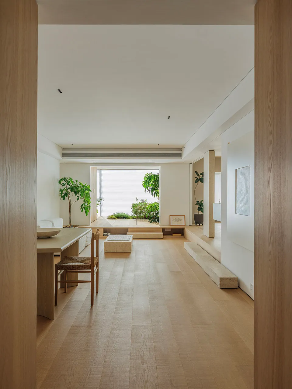 A modern minimalist living room with wooden floors, minimal furniture, and natural light.
