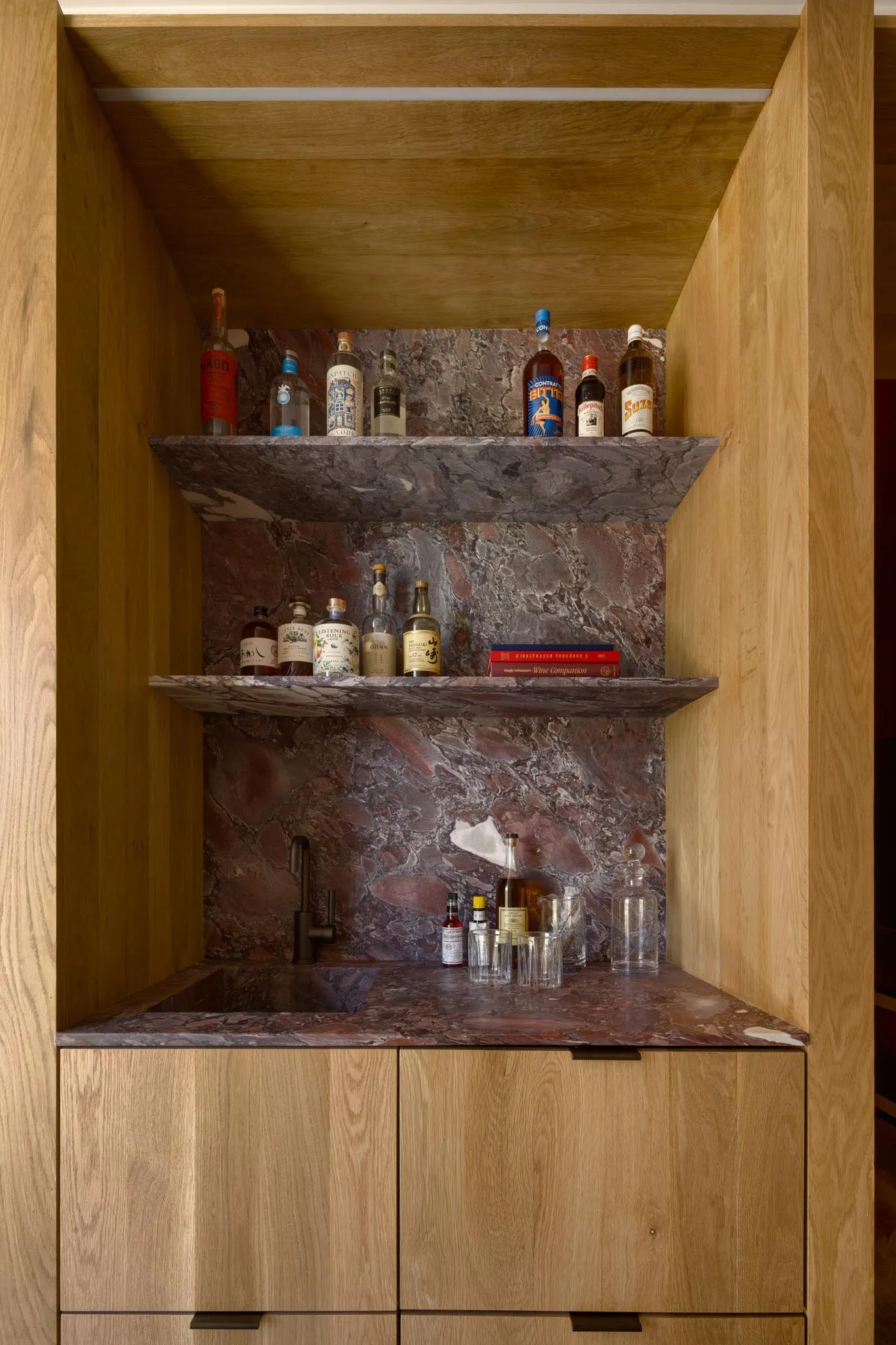 A home bar with wooden shelves and a marble countertop displaying various bottles of liquor and glasses.
