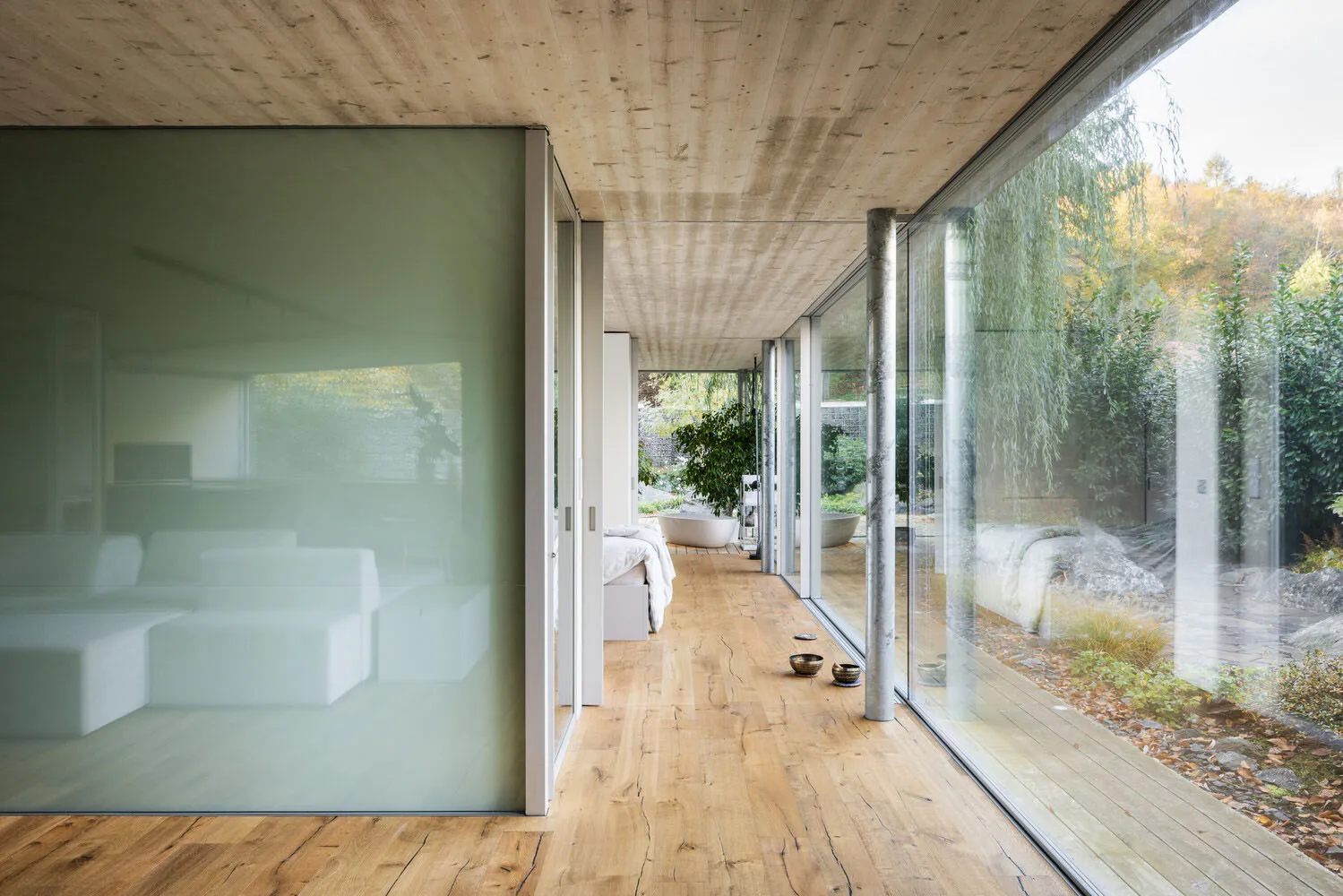 Modern living room with glass walls, wooden floors, and a view of the garden.