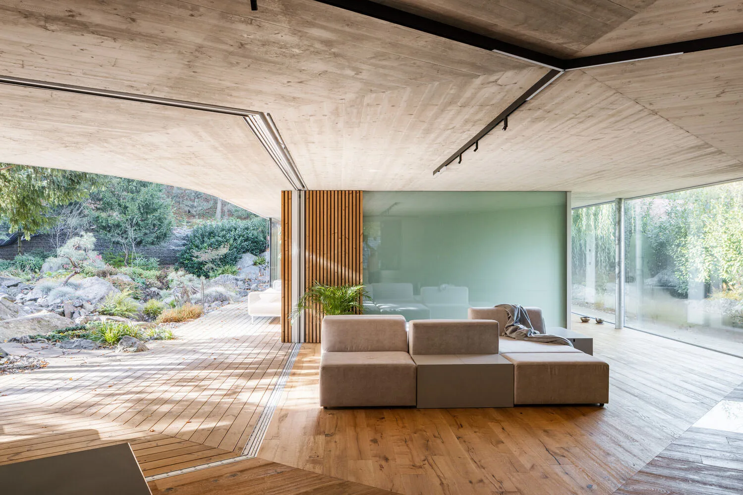 Interior of a modern living room with wooden walls and floor, large windows, and minimalist furniture.