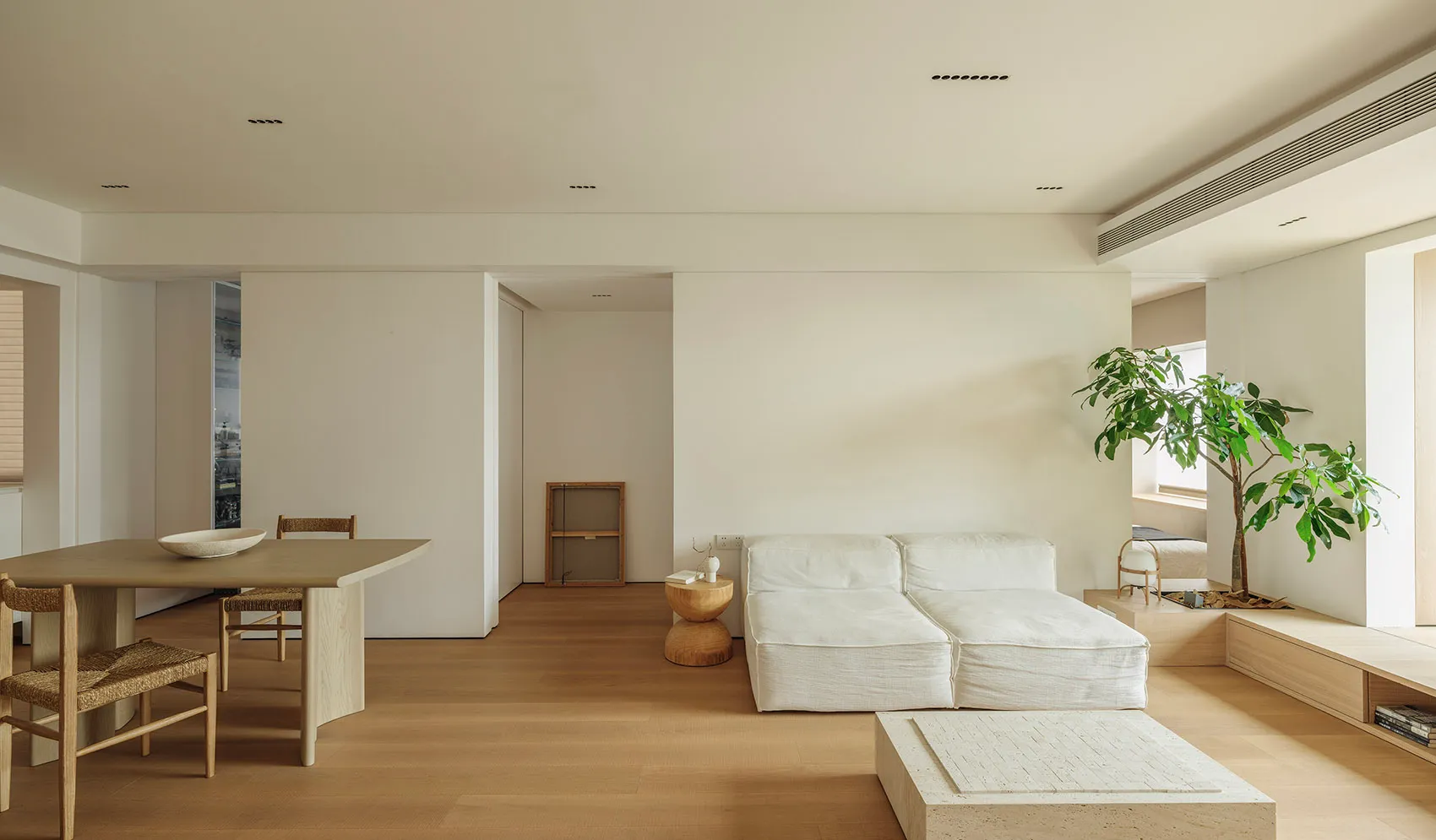 A minimalist living room featuring a white sofa, wooden coffee table, and green plant