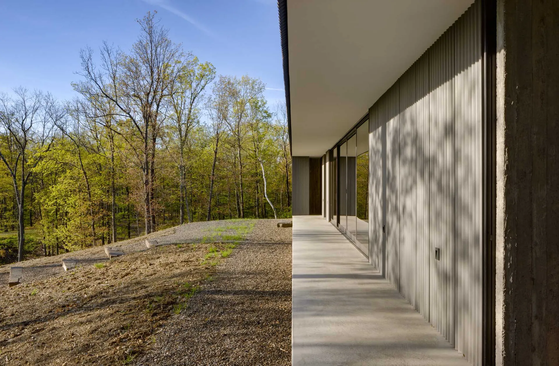 Modern residential building exterior with metal siding and large windows overlooking a forested area.