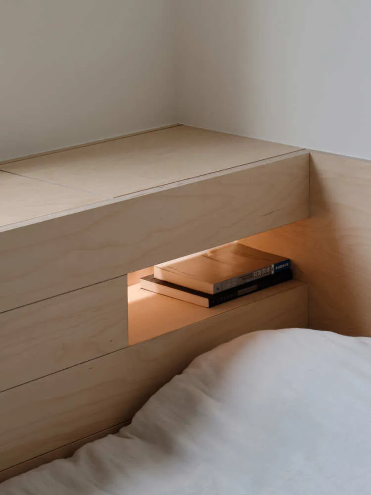A minimalistic bedroom featuring a built-in nightstand made of light-colored wood.