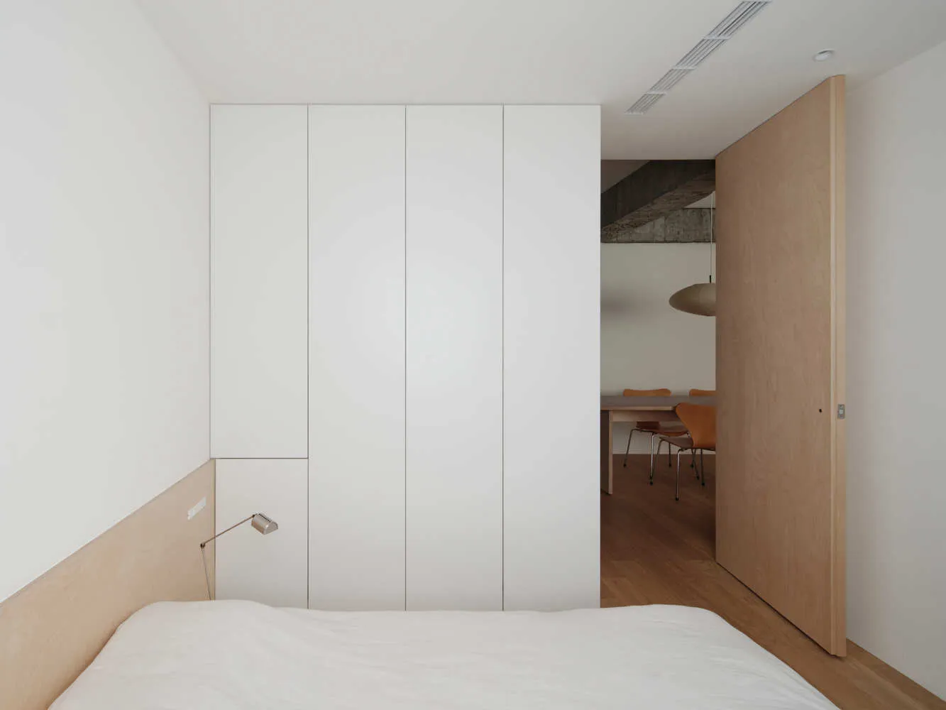 A minimalist bedroom featuring a wooden bed and a white wardrobe.