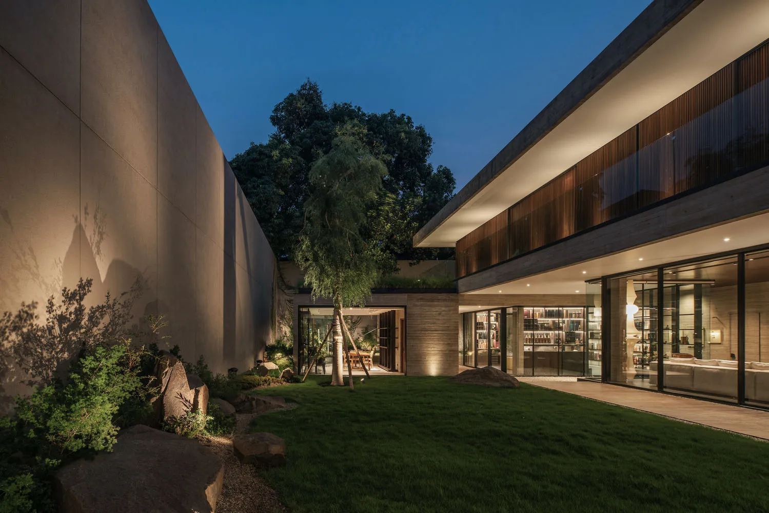 A modern residential exterior with concrete walls, a grassy courtyard, and a tree.