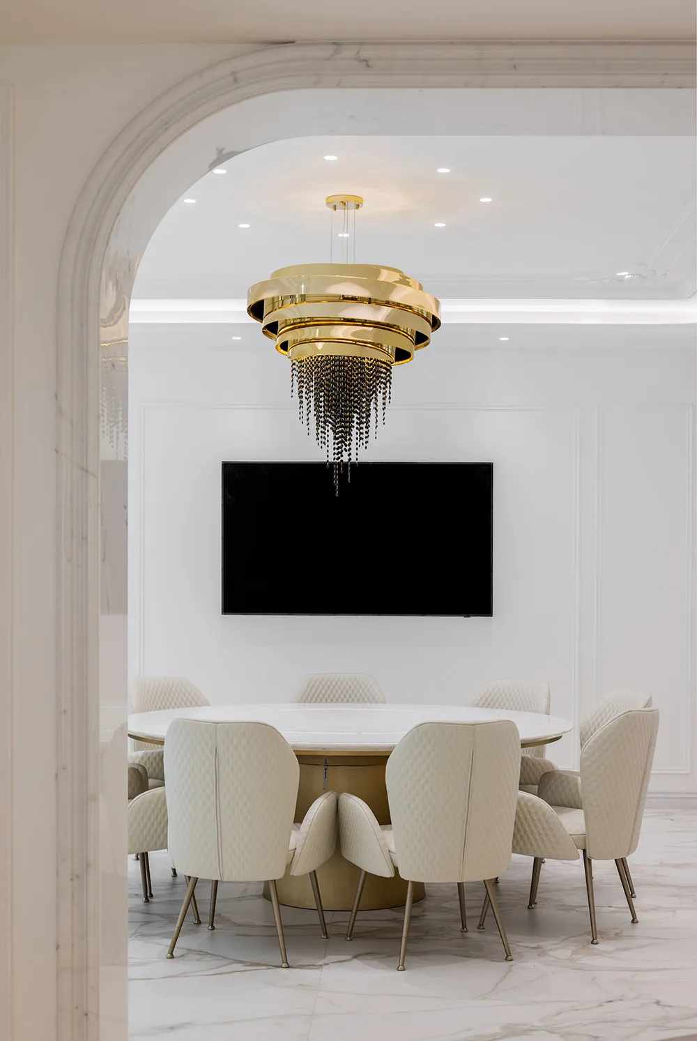 A modern conference room with a circular table, white chairs, and a white marble finish.