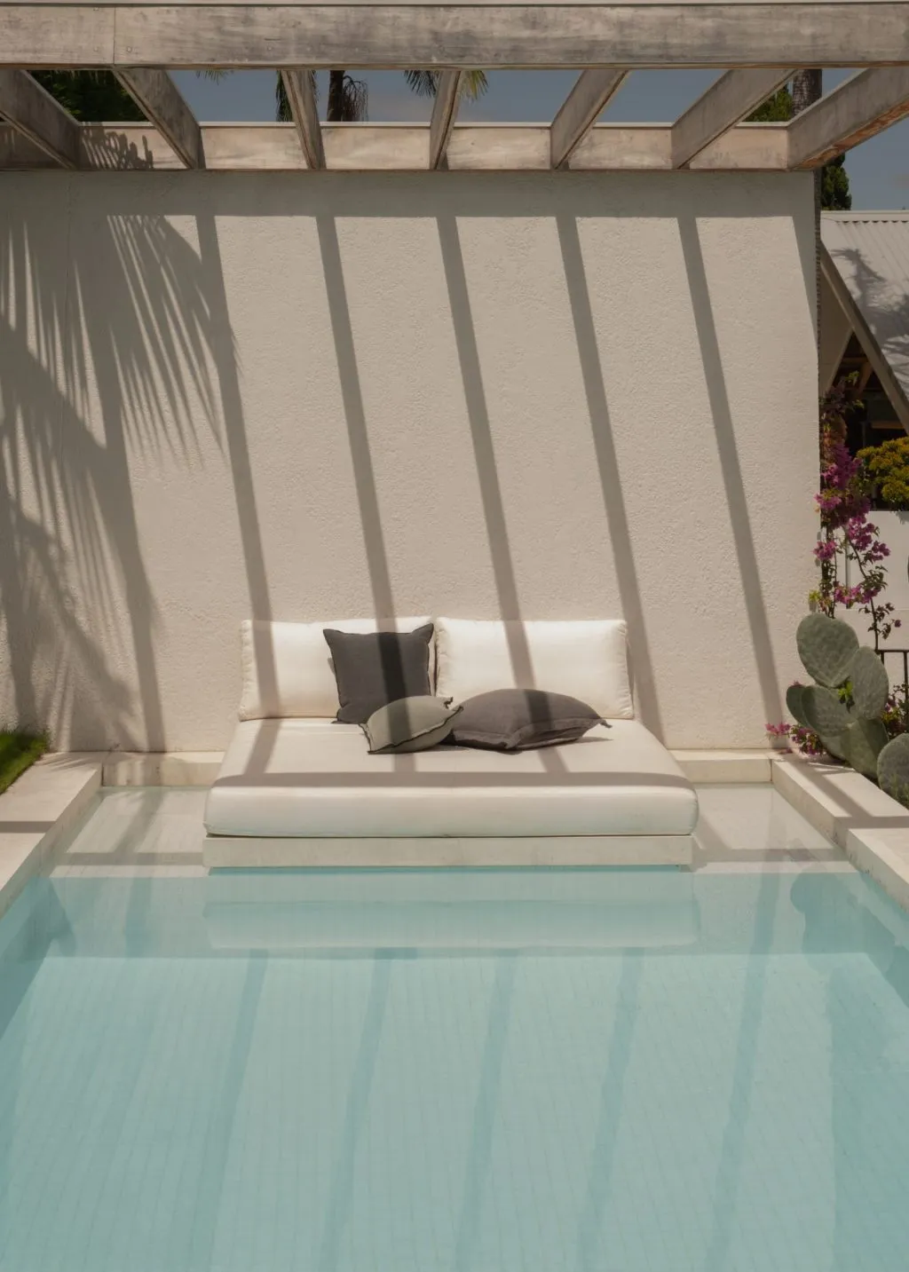 A modern poolside lounge with concrete flooring and a wooden pergola structure.