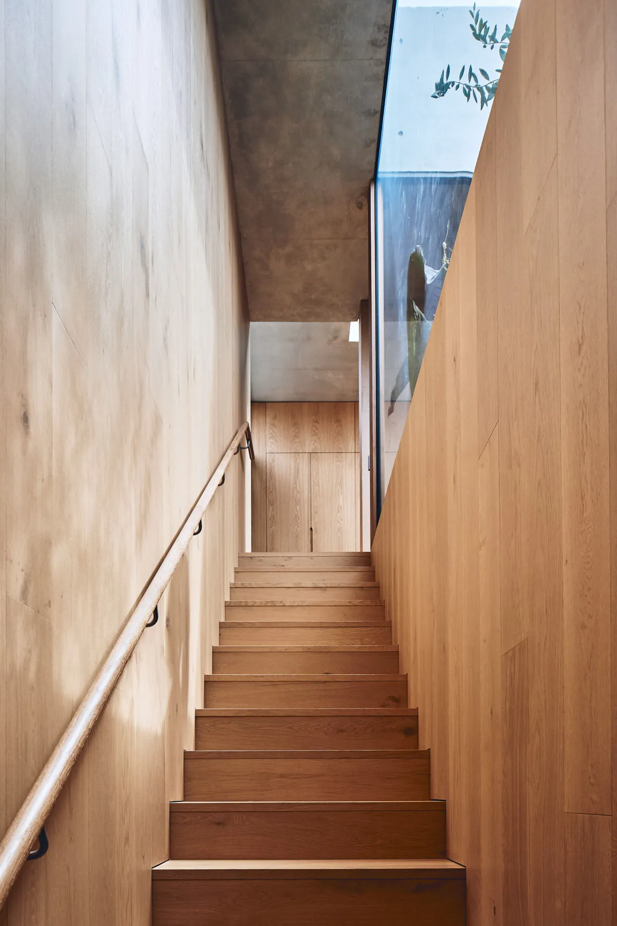 An image showing a modern wooden staircase with concrete walls in a minimalist industrial design.
