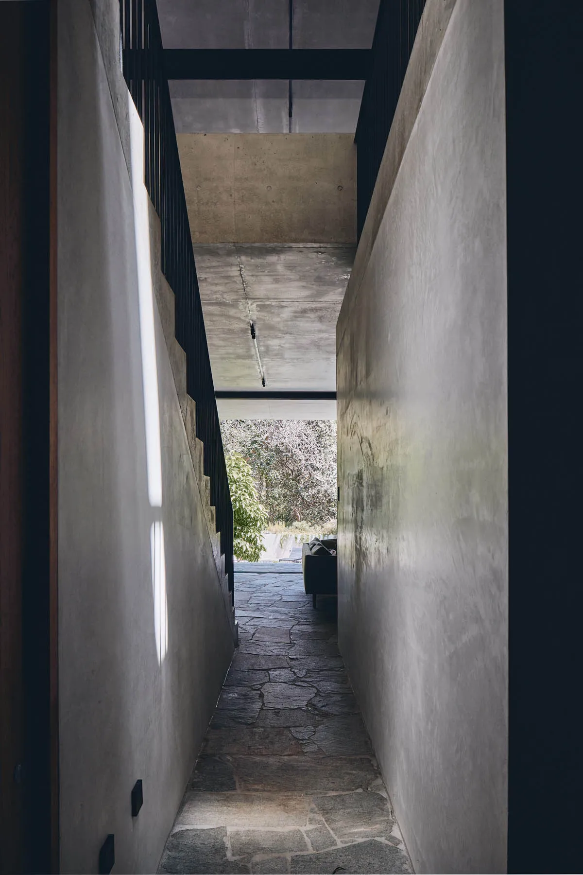 A narrow concrete hallway with stone flooring and a view of the outdoors.