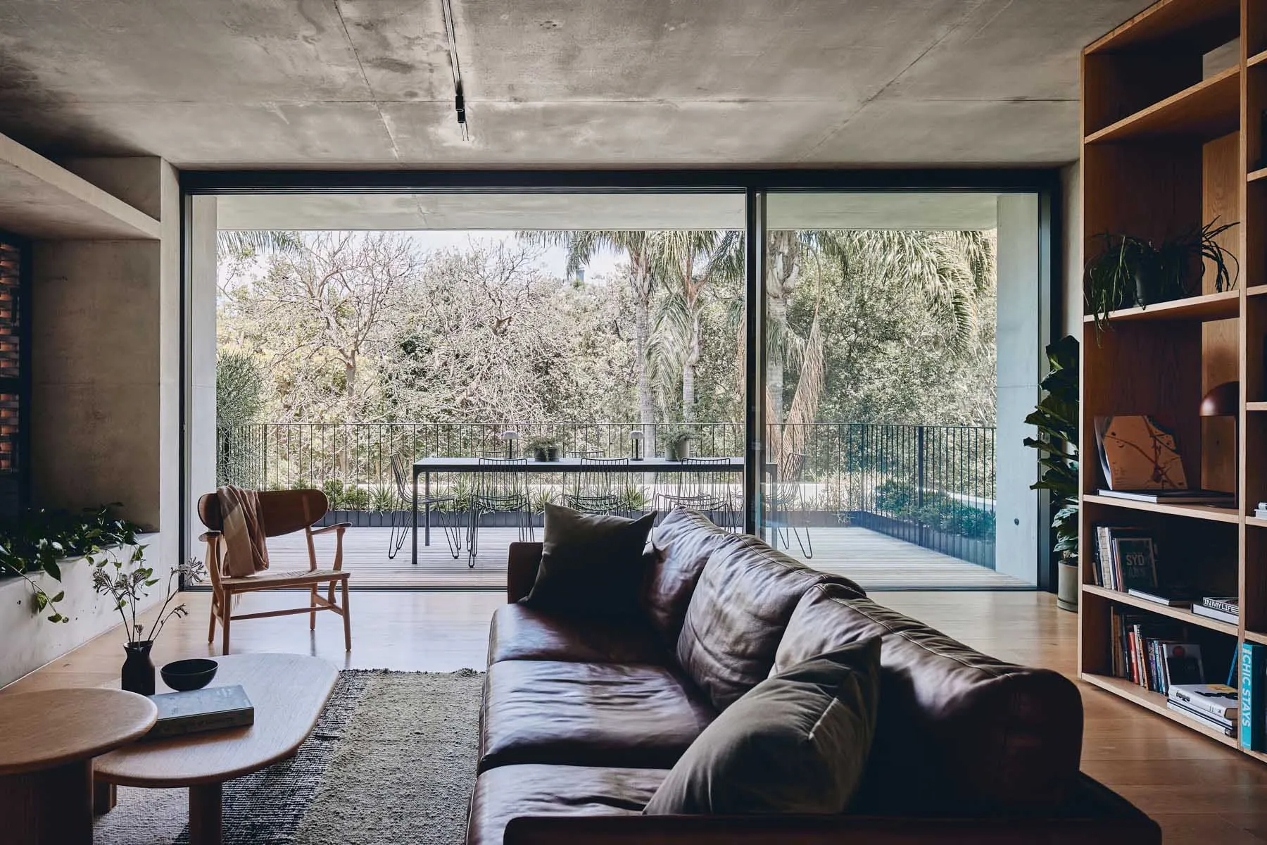 A modern living room featuring a concrete ceiling, a leather sofa, a wooden coffee table, and a bookshelf filled with books a
