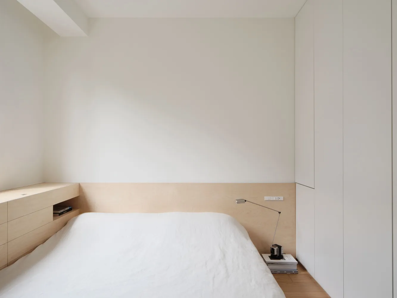Minimalist bedroom with a white platform bed, wood floor, and white walls.