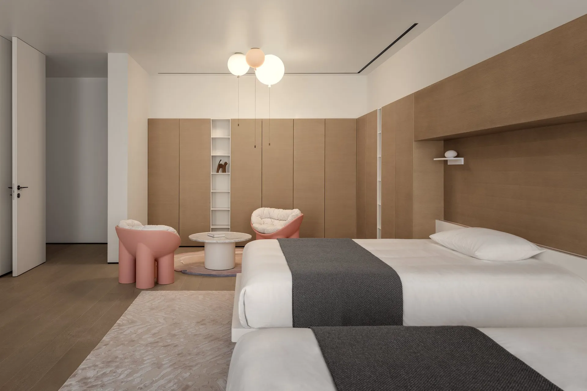 Modern minimalist bedroom with wooden walls and built-in cabinets, featuring a pink accent chair and table, and a comfortable