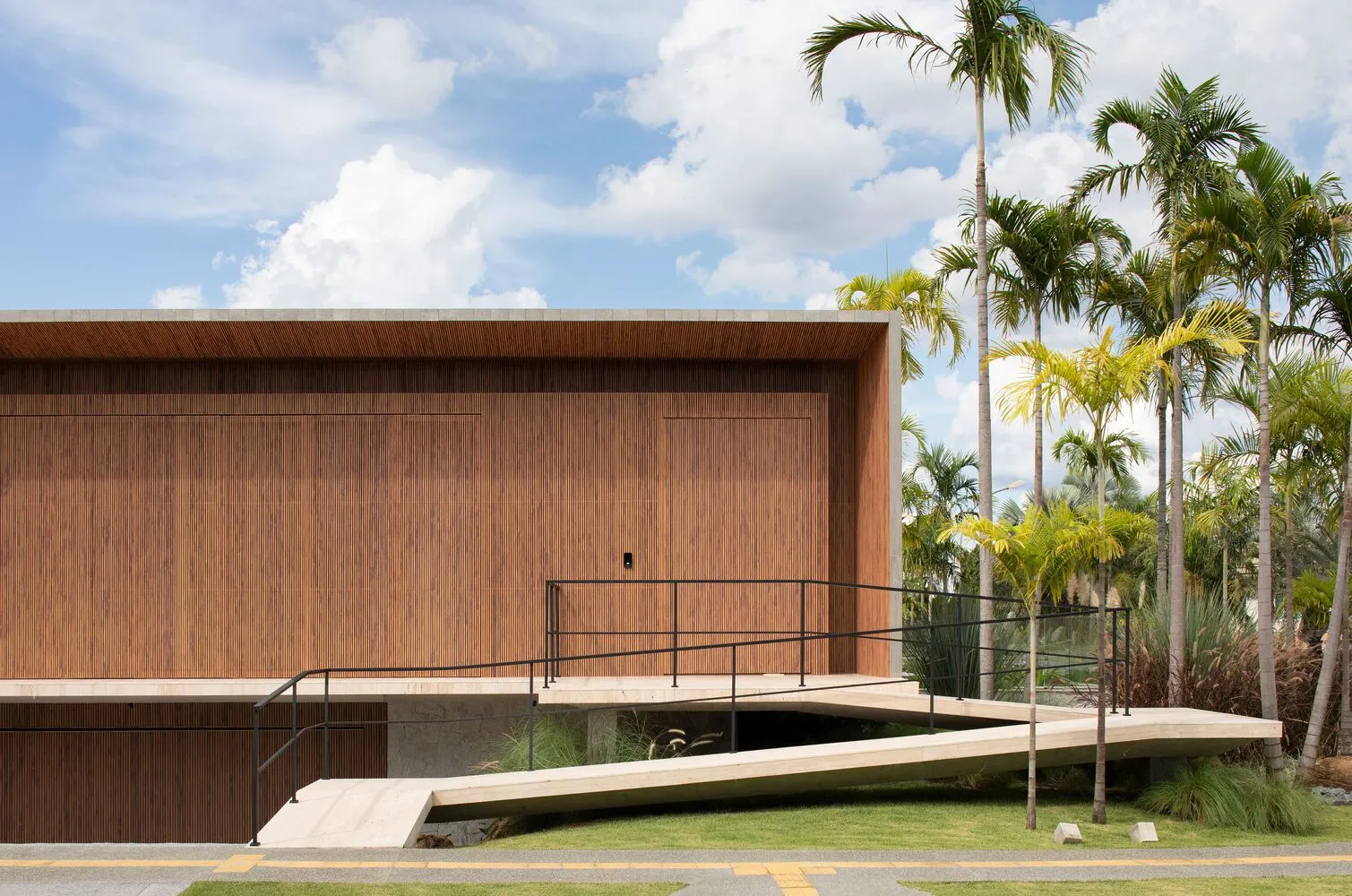Modern library exterior made of wood with a ramp and palm trees.