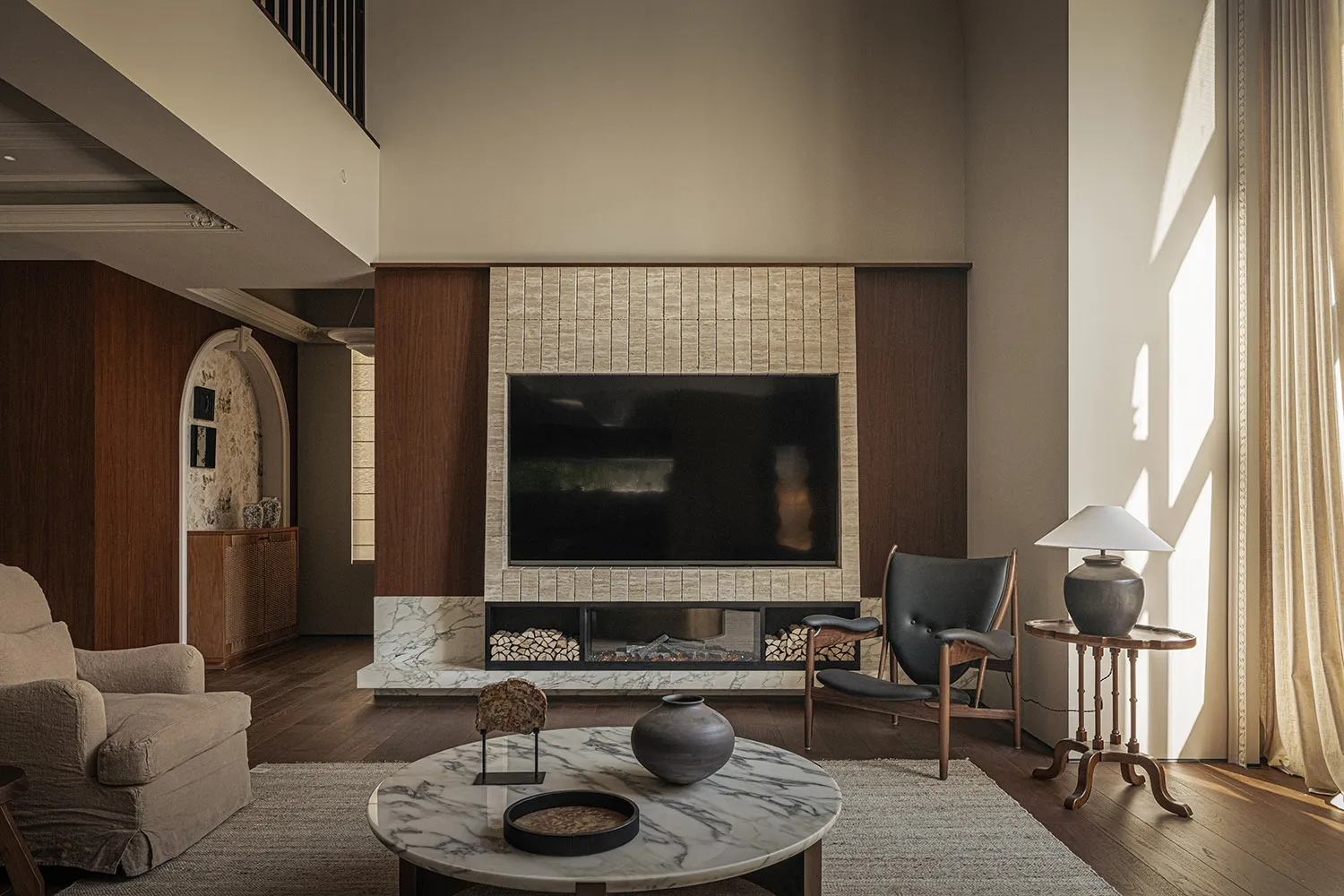 A modern living room features sleek, minimalist furnishings with a marble coffee table, wooden chairs, and a tile fireplace.