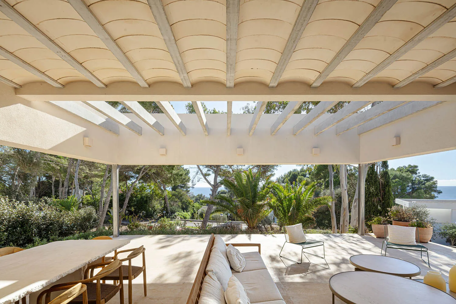 Modern minimalist outdoor living space with white lounge furniture, wooden table, and greenery.