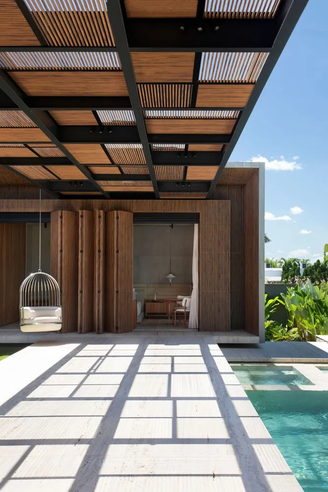 Swimming poolside lounge area with modern wooden and concrete patio furniture, under a wooden slat ceiling.