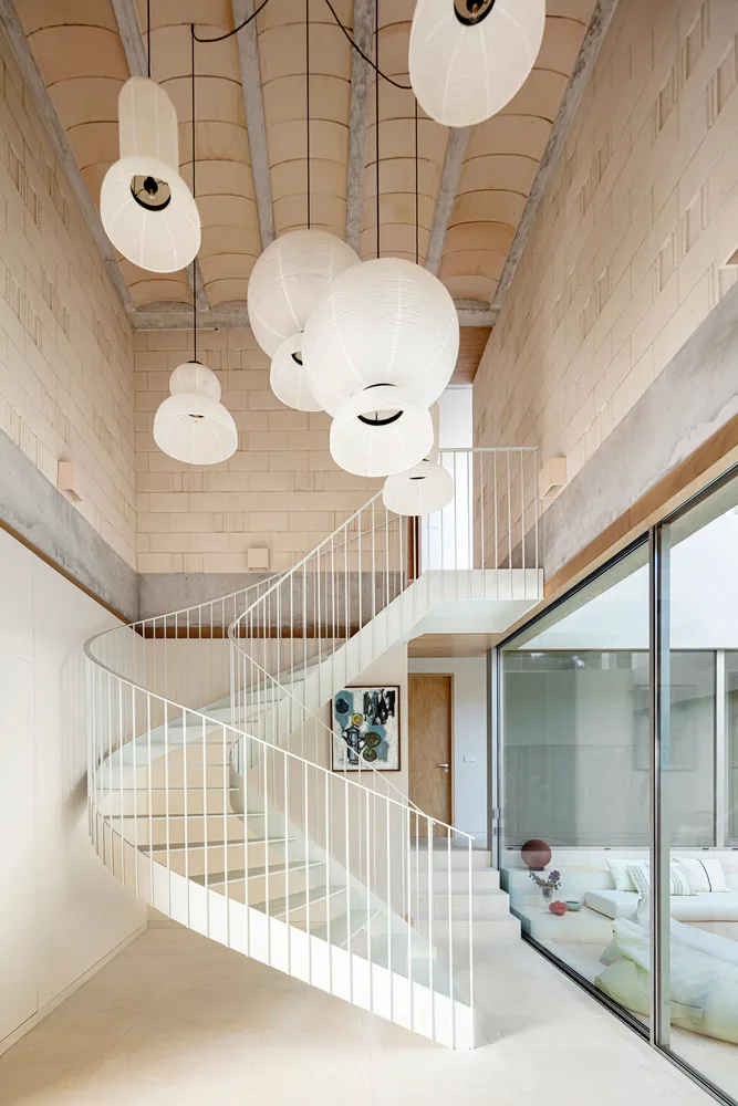 Modern residential interior featuring a spiral staircase adorned with hanging paper lanterns, complemented by a concrete ceil