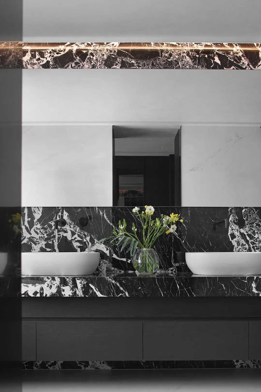 Modern minimalist bathroom with black marble countertops, white sinks, and floral decoration.