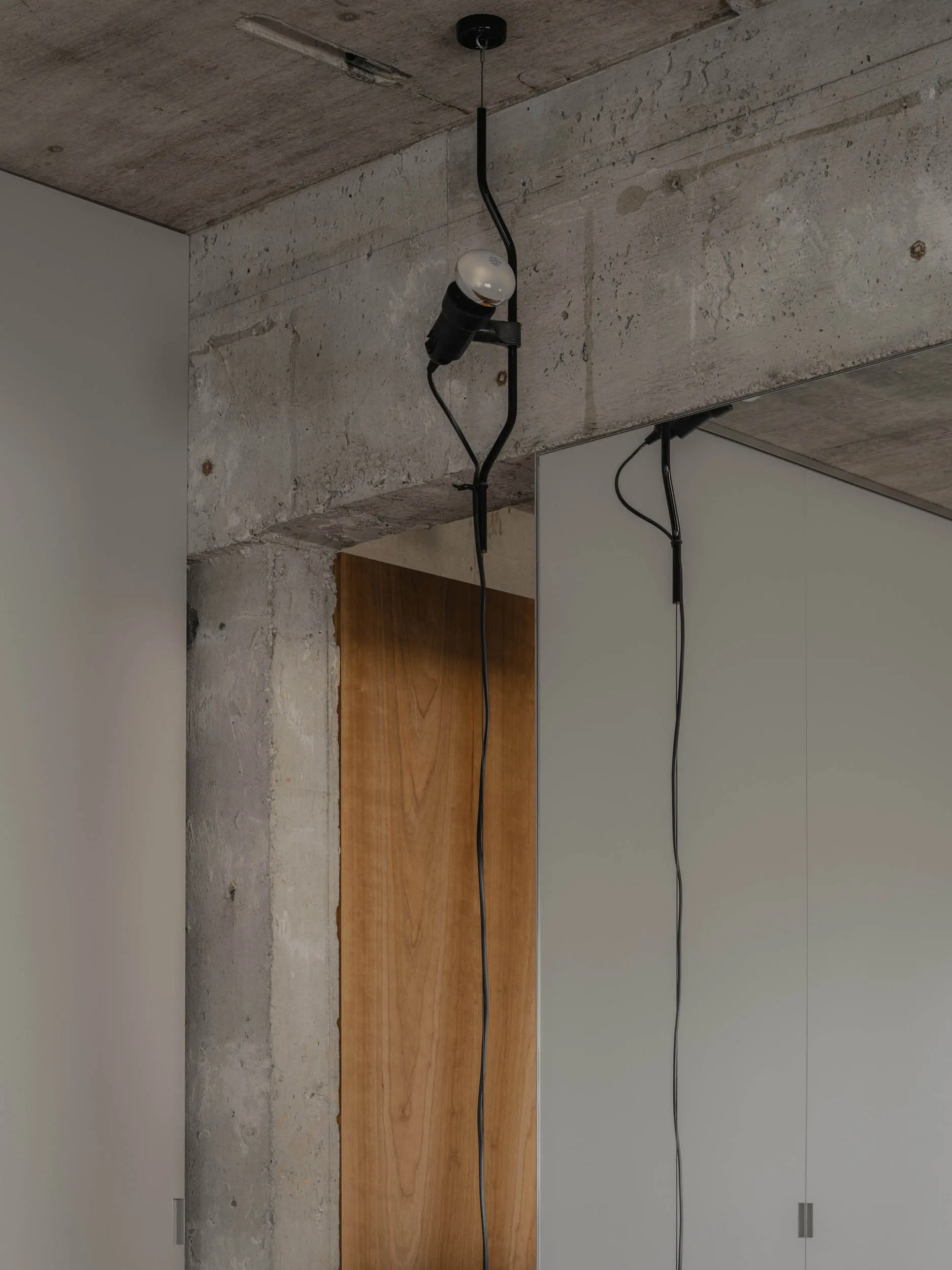 A minimalist concrete interior with a hanging light fixture and a wooden door.