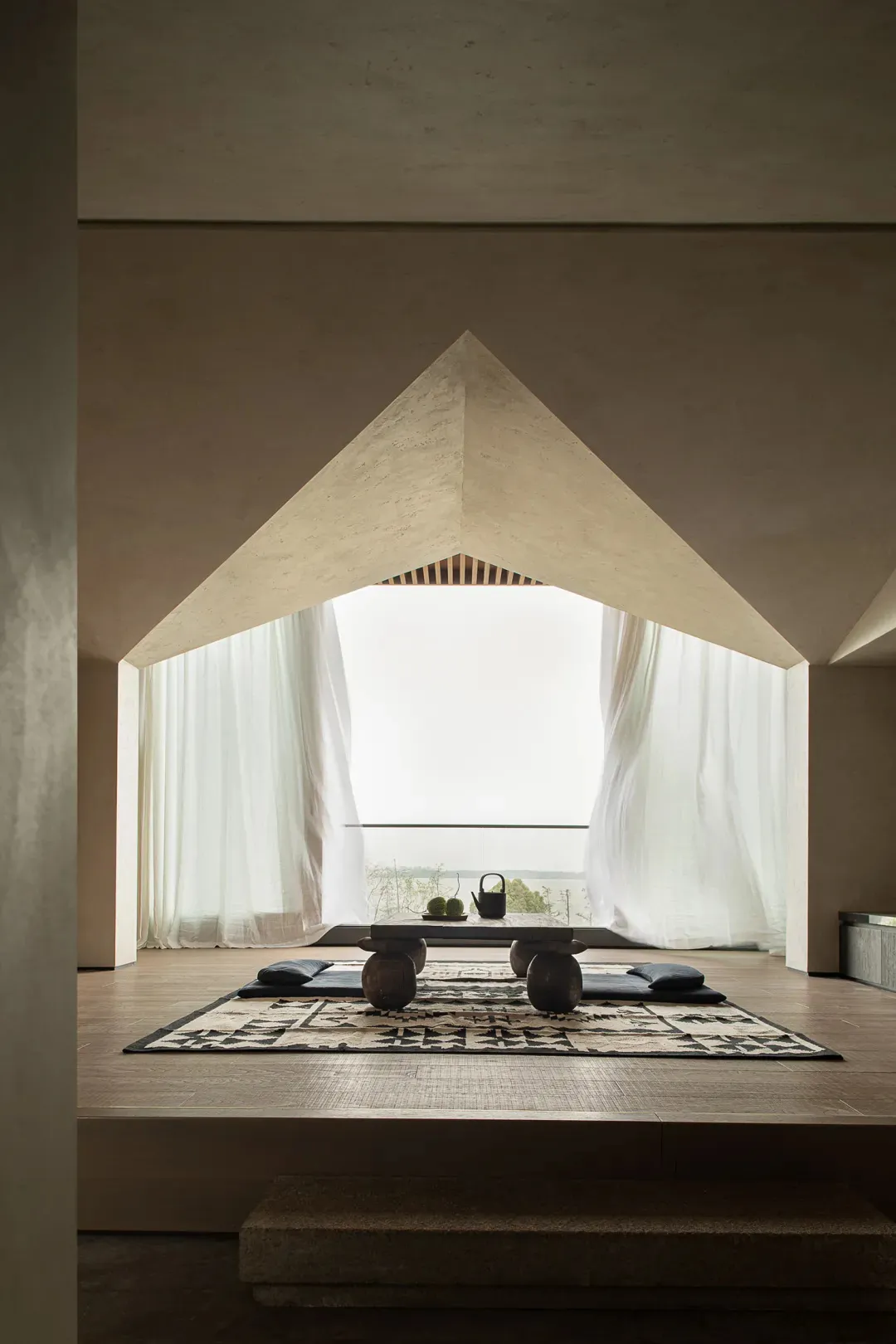 Modern minimalist living space featuring a concrete floor and a large window overlooking a serene landscape.