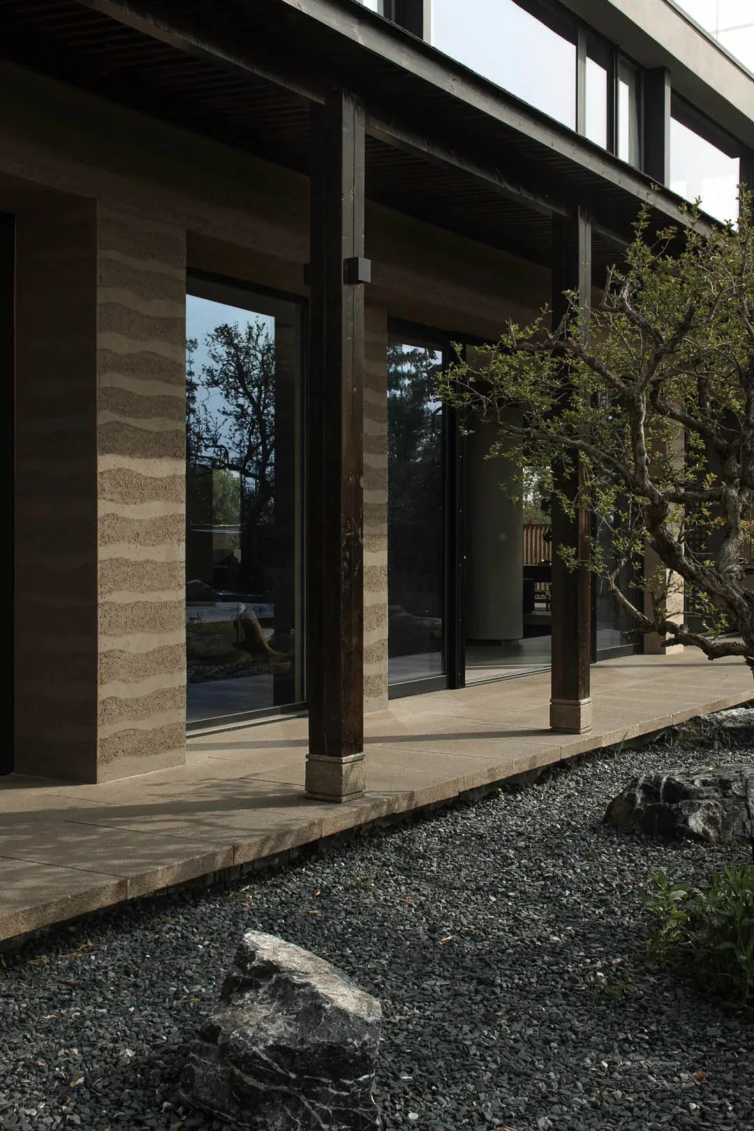 Modern house exterior with concrete and wooden columns and a gravel garden with rocks and plants.
